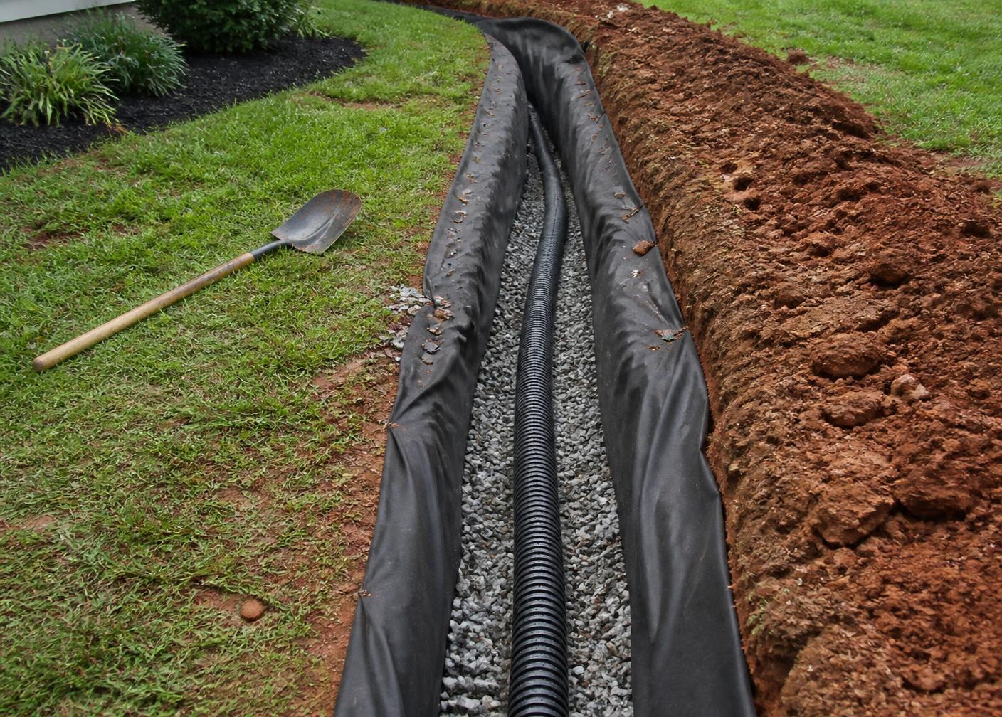 Perforated drainage pipe and washed gravel in a fabric-lined French drain trench